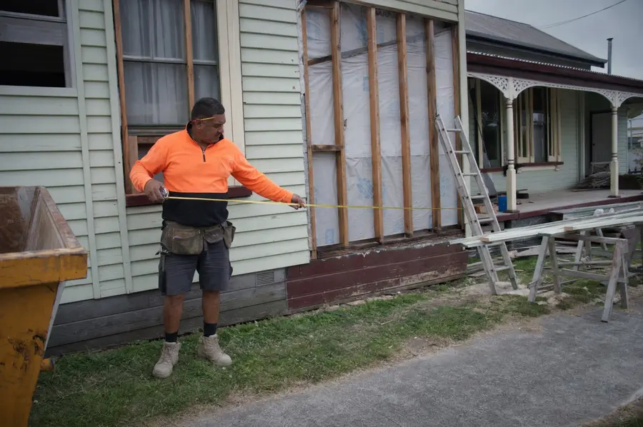 Builder taking measurements against the framing of a partly built house on a Christchurch section