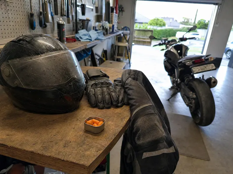 Motorcycle helmet, leather jacket and gloves laid out on a garage workbench in a New Zealand home