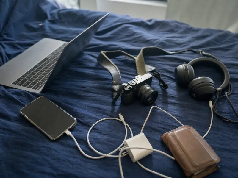 Laptop, phone, headphones and camera laid out on a bed in a Wellington flat