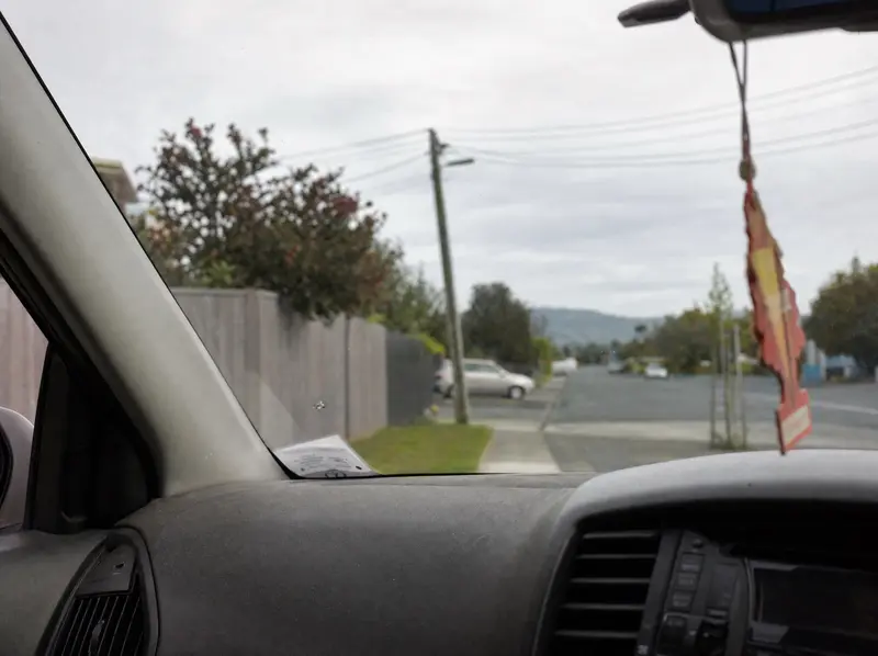 Star-shaped stone chip in a windscreen seen from the passenger seat, suburban street blurred beyond