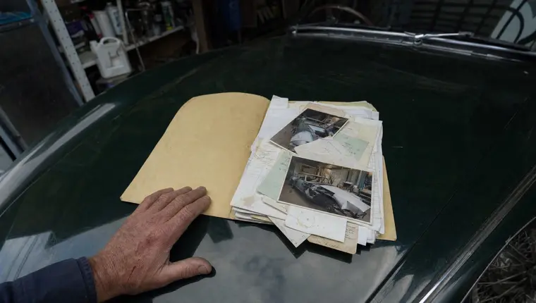 Restoration receipts and photographs spread on the bonnet of a classic car, supporting an agreed value