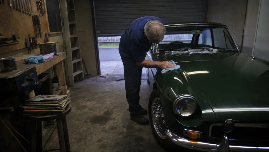 Owner wiping down the front wing of a restored 1960s classic car in a home garage