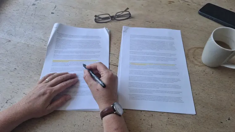 Overhead view of hands comparing two printed policy schedules, a pen resting against one line