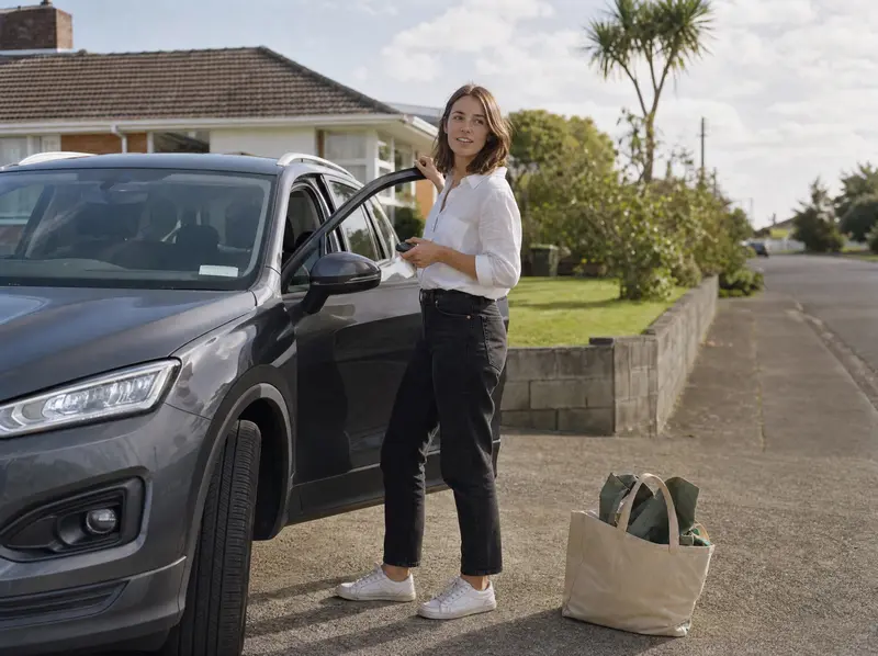Woman standing beside her car on a quiet New Zealand suburban street on a clear autumn morning